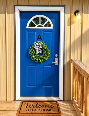 A blue door with a white letter 'A' above it, a black and white checkered bow, and a green wreath. - The Meadow Lodge- Cozy 3BR Farm Barndo with Fire Pit and nearby Wedding Venues  (White Hall)