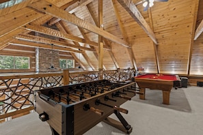 Un espace de loisirs intérieur doté de poutres en bois, d’un baby-foot et d’une table de billard.