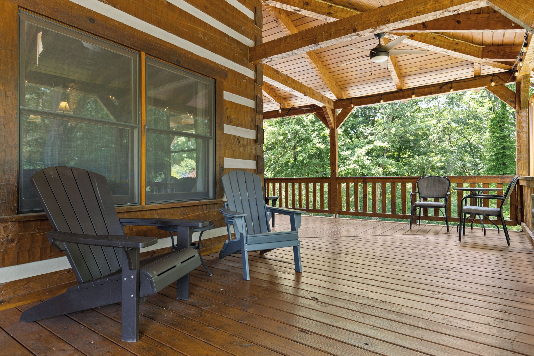 Una terraza de madera con sillas Adirondack y una mesa, con vista a un área boscosa.