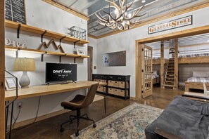 A room with a desk, chair, bunk beds, a television, and a chandelier. - Waterfall Pool · Barrel Sauna + Hot Tub · Cabin · 15 Private Acres (Mineral Bluff)