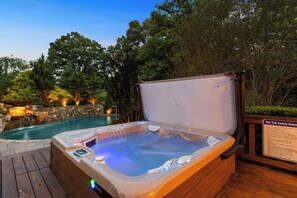 Un bain à remous avec une terrasse en bois, un mur en pierre et un panneau indiquant les règles de sécurité.