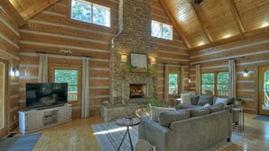 L’intérieur d’une cabane en rondins, avec une cheminée en pierre, un grand téléviseur et un coin salon confortable.