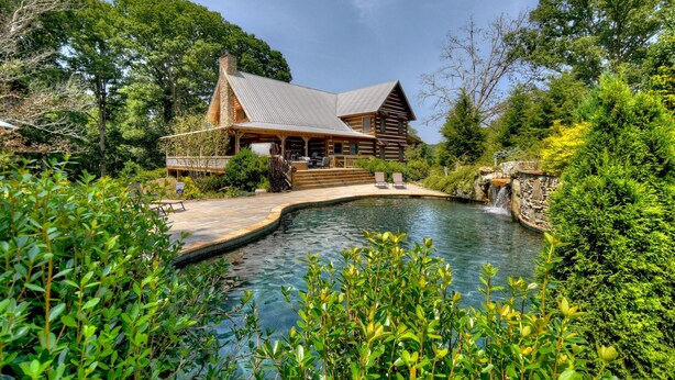 Une cabane en rondins avec une piscine, le tout entouré d’une végétation luxuriante.