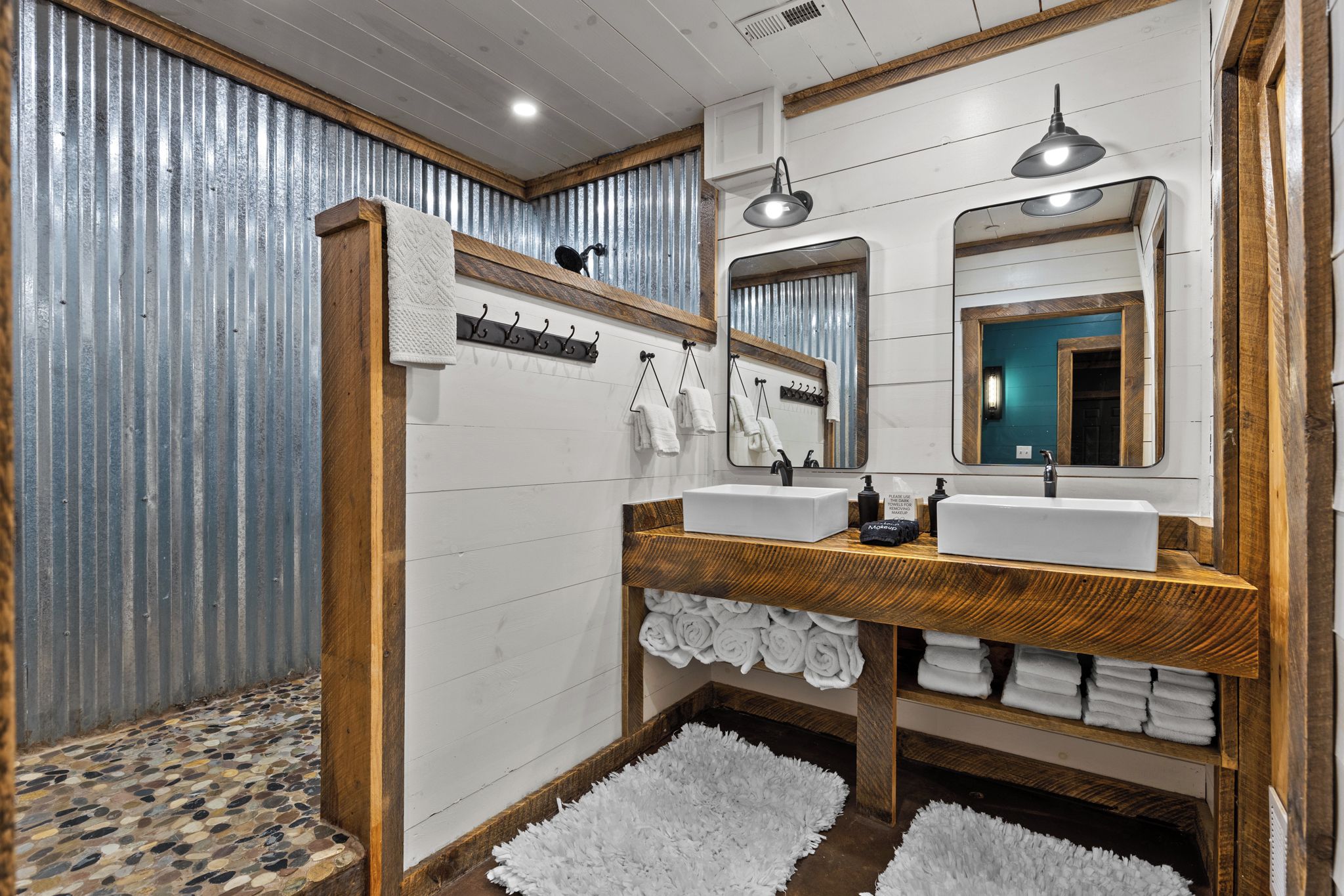Un baño con tocador de madera, dos lavamanos, un espejo y zona de ducha.