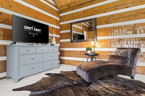 A room with a television on a dresser, a mirror, a sofa, and a rug. - Waterfall Pool · Barrel Sauna + Hot Tub · Cabin · 15 Private Acres (Mineral Bluff)