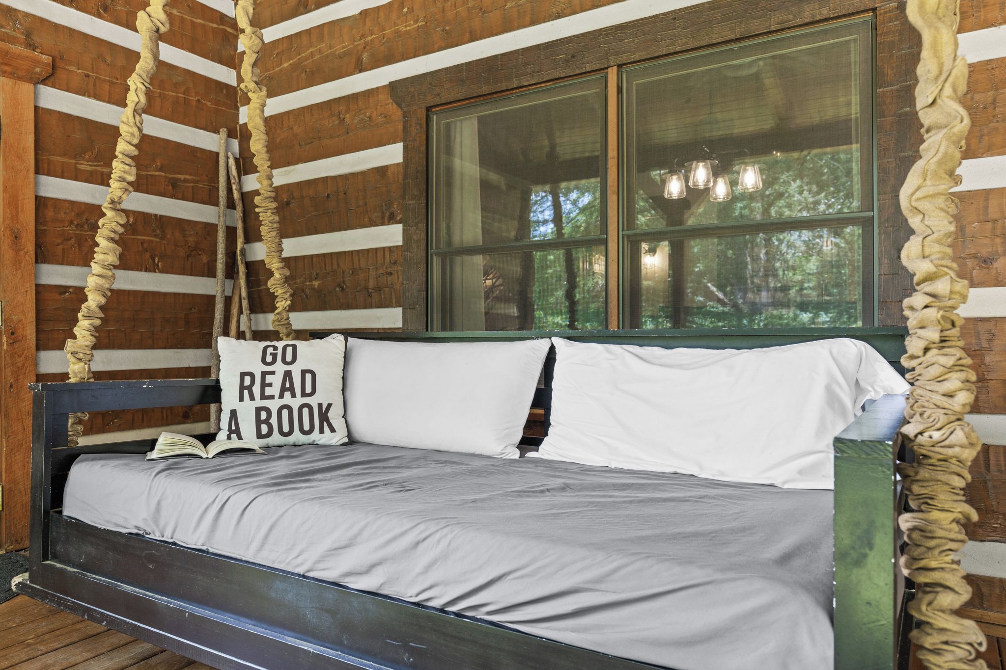 Uma cabana rústica de madeira com uma cama e um travesseiro com a frase 'GO READ A BOOK'.