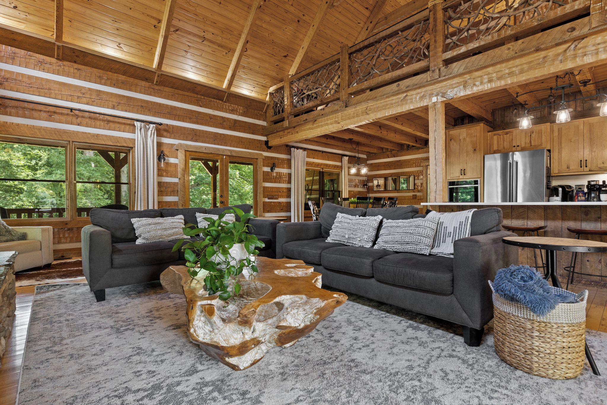 A spacious living room with a large gray sofa, a coffee table with a unique wooden design, and a view of the kitchen area.