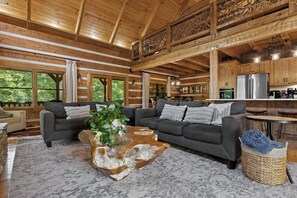 A spacious living room with a large gray sofa, a coffee table with a unique wooden design, and a view of the kitchen area.