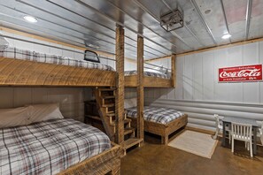 A bunk bed room with a ladder, a Coca-Cola sign, and a small table with chairs.