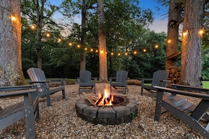 Un hogar rodeado de sillas Adirondack, luces colgantes y árboles.