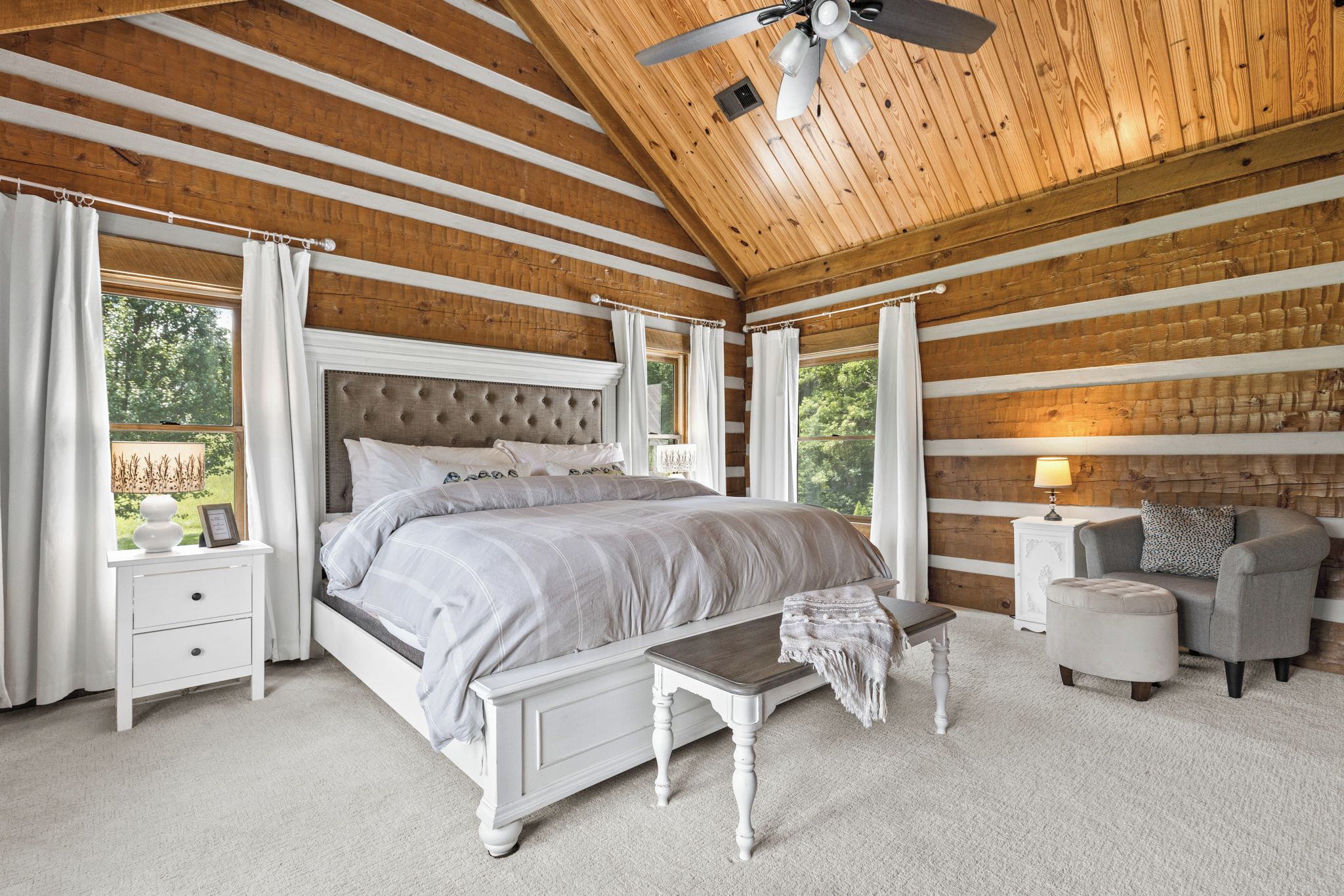 A bedroom with a large bed, a bedside table, a bench, a nightstand, and a lamp.