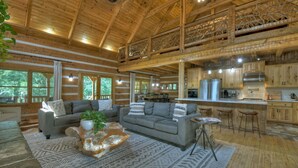 Un intérieur spacieux de chalet en bois, comprenant un grand salon, une cuisine et un balcon.