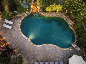A swimming pool with a stone border, surrounded by a paved patio and lounge chairs. - Waterfall Pool · Barrel Sauna + Hot Tub · Cabin · 15 Private Acres (Mineral Bluff)
