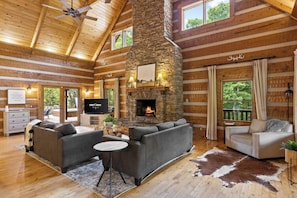 L’intérieur d’une cabane en rondins, avec une cheminée en pierre, des canapés en cuir, un téléviseur et un plafond en bois.