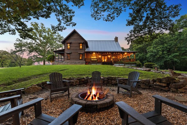 A log cabin with a fire pit and Adirondack chairs in the foreground.