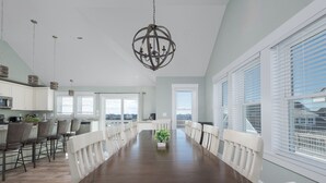Un vaste espace dédié à la salle à manger, avec une longue table en bois, des chaises blanches et un lustre.