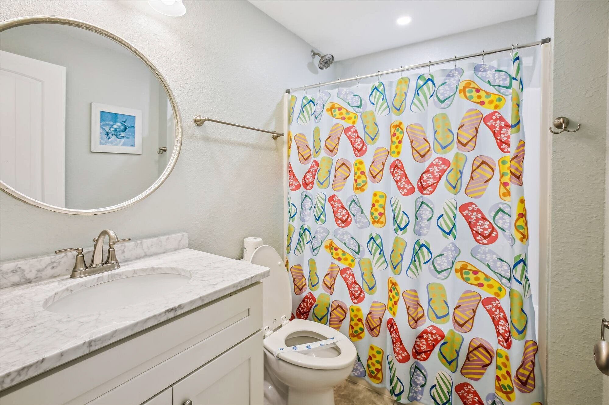 A bathroom with a white marble sink, a toilet, and a shower curtain with a colorful pattern.
