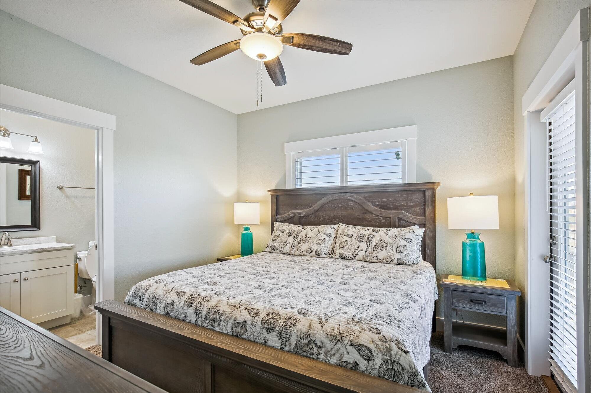 A bedroom with a bed, nightstands, a ceiling fan, a window, and a door.