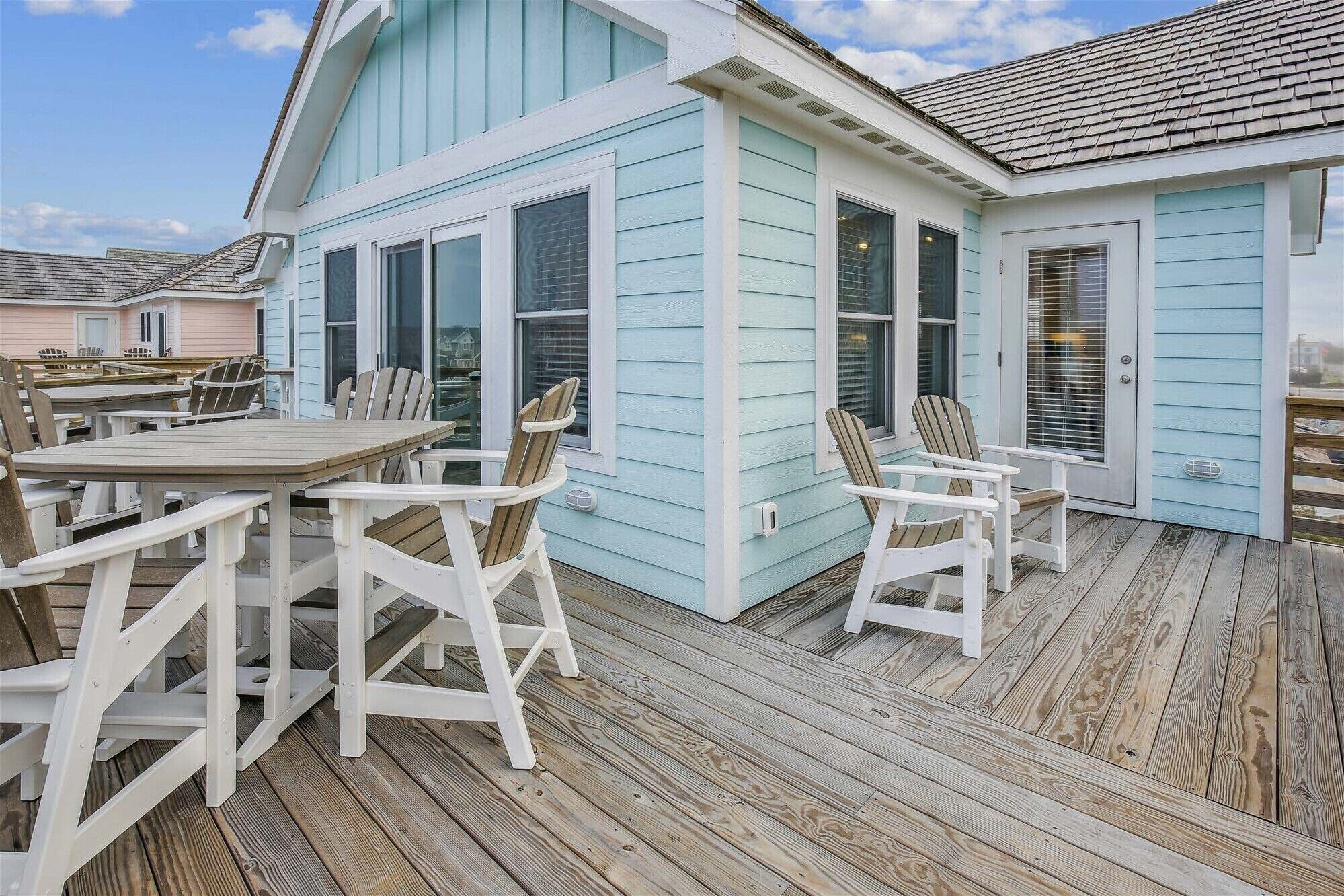 Une terrasse en bois avec des sièges d’extérieur et un bâtiment dont le revêtement est d’un bleu clair.
