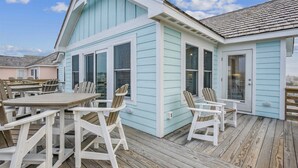 Une terrasse en bois avec des sièges d’extérieur et un bâtiment dont le revêtement est d’un bleu clair.