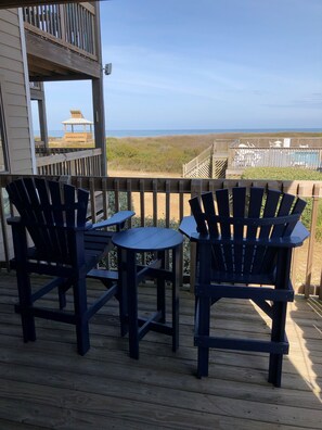 Een houten terras met twee Adirondack-stoelen en een kleine tafel, met uitzicht op een strand en een zwembad.