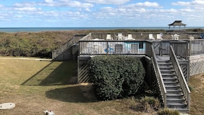 Eine Holzterrasse mit einer Treppe zu einem überdachten Bereich, umgeben von einem Zaun und Blick auf den Strand.