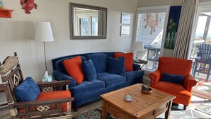 Ein Wohnzimmer mit blauem Sofa, orangefarbenem Sessel, Couchtisch aus Holz und einem gemusterten Teppich.