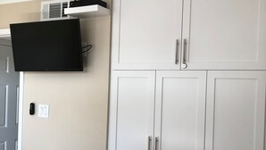 Ein Zimmer mit einem weißen Kleiderschrank, einem an der Wand befestigten Flachbildfernseher und einer Steckdose.