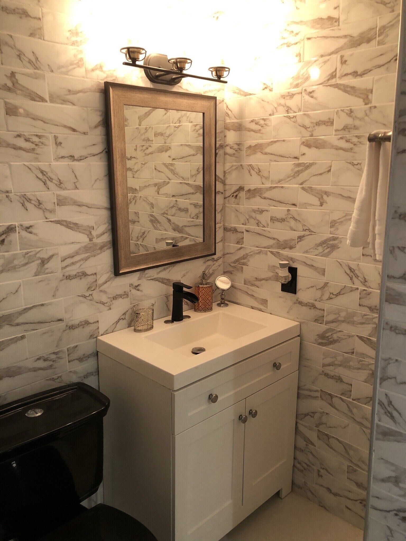 Une salle de bain avec un mur aux motifs de marbre, un lavabo blanc doté de deux robinets, un miroir et un porte-serviettes.