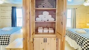 A wooden cabin room with a central cabinet containing towels, a bed with checkered bedding, and a small table.