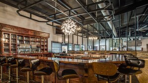 A bar area with a wooden bar, multiple stools, and a large chandelier.