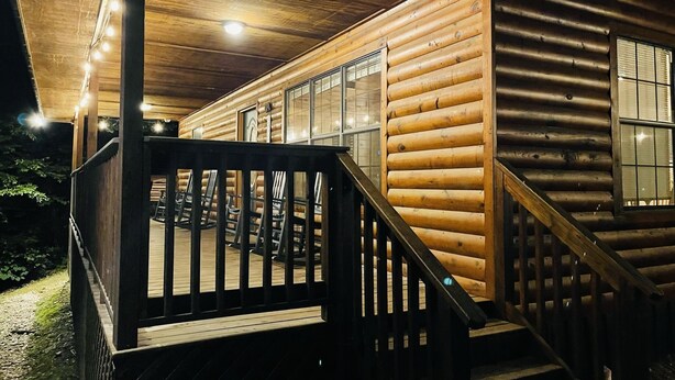 A log cabin with a wooden deck, a staircase, and a railing.