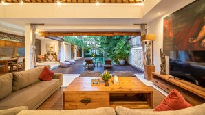 A spacious living area with a wooden coffee table, sofas, and a TV. There is a dining area with a table and chairs visible in the background. - Fabulous Private Villa, 3 BR, Canggu With Staff (Tibubeneng)