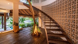 Una escalera en espiral con acabado de madera, rodeada por un enrejado decorativo y una estructura de techo de paja.