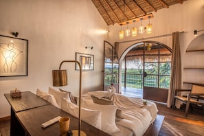 A cozy room with a bed, a wooden table, and a large window offering a view of the outdoors.