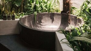 A concrete water feature with a metal structure, surrounded by lush green plants and a thatched roof overhead.