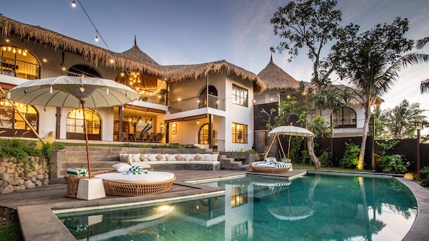 A resort with a swimming pool, outdoor seating, and thatched-roof buildings.