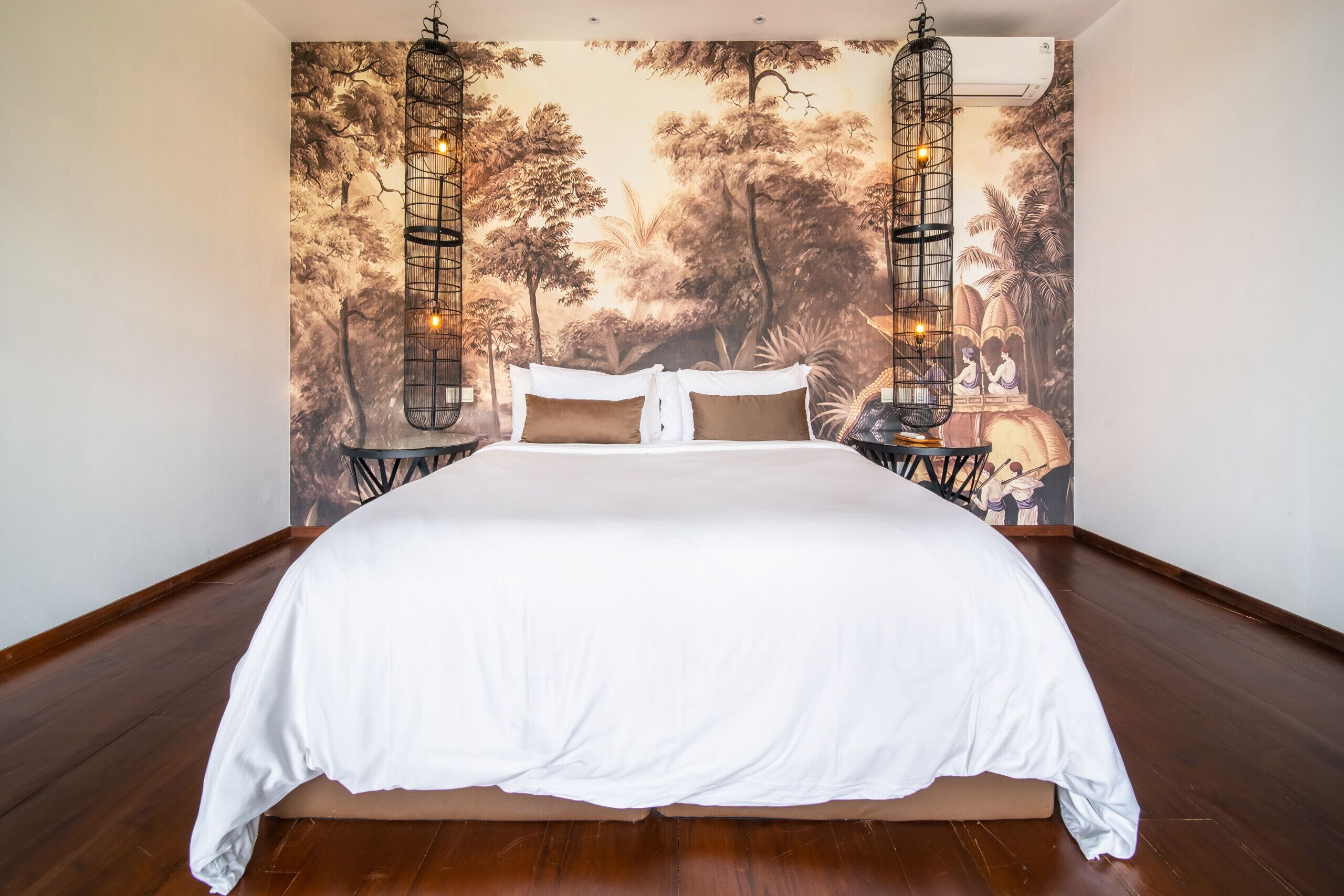 A large bed with white bedding in a room with a mural of trees and birds on the wall.