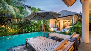A poolside area with lounge chairs and an umbrella, surrounded by lush greenery and a modern house. - Splendid Private Villa, 4 BR, Canggu With Staff (Pererenan)