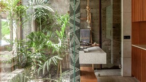 A modern bathroom with a glass shower enclosure, a wooden bench, and a variety of plants. - Batukaru Private Pool Suite 2 (Canggu)