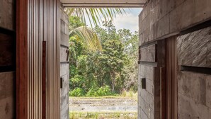 A corridor with wooden slats and a concrete ceiling leading to an outdoor area with greenery. - Batukaru Private Pool Suite 2 (Canggu)