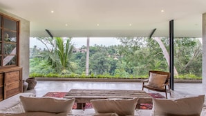 A spacious room with a large window overlooking a lush garden, a wooden bench, and a sofa with cushions. - Exceptional 2 BR Suites in Ubud Hidden Gem (Ubud)