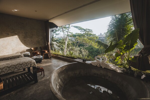 A room with a large bathtub, two beds, and a view of a tropical landscape.
