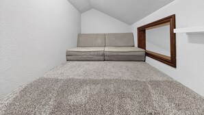 A small, enclosed room with a grey carpet, a grey sofa, and a wooden-framed mirror on the wall.