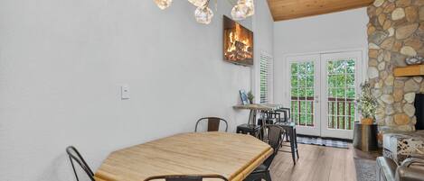 A dining area with a wooden table and chairs, a chandelier, and a stone fireplace.