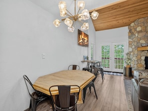 A dining area with a wooden table and chairs, a chandelier, and a stone fireplace.
