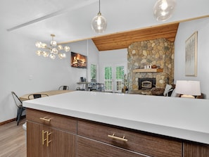 A modern kitchen with a large island, stone fireplace, and pendant lighting.
