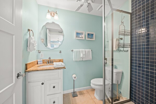 A bathroom with a white vanity, a round mirror, a toilet, and a shower area with a glass door.