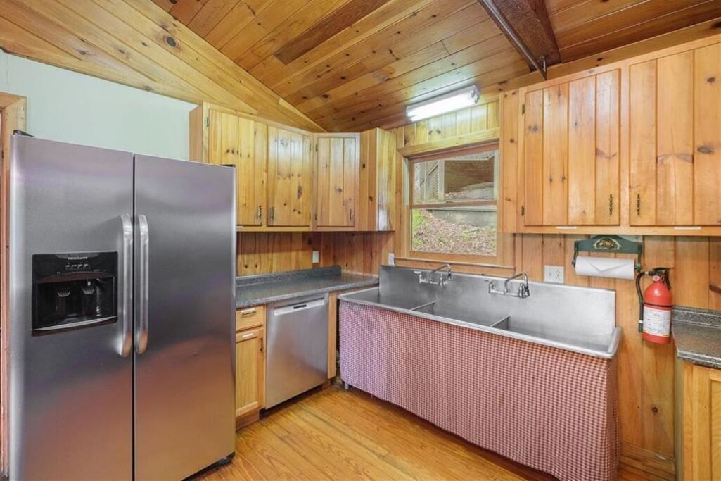 A kitchen with wooden cabinets, a stainless steel refrigerator, a sink, and a window with a view of the outdoors.