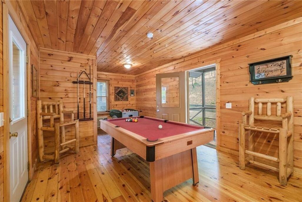 Une cabane en bois avec une table de billard, des chaises en bois et une échelle.